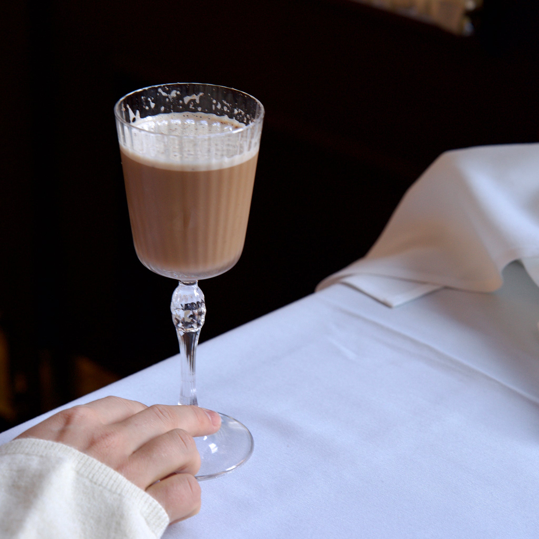 Glass of fall cocktail held by a hand on a white surface with a dark background