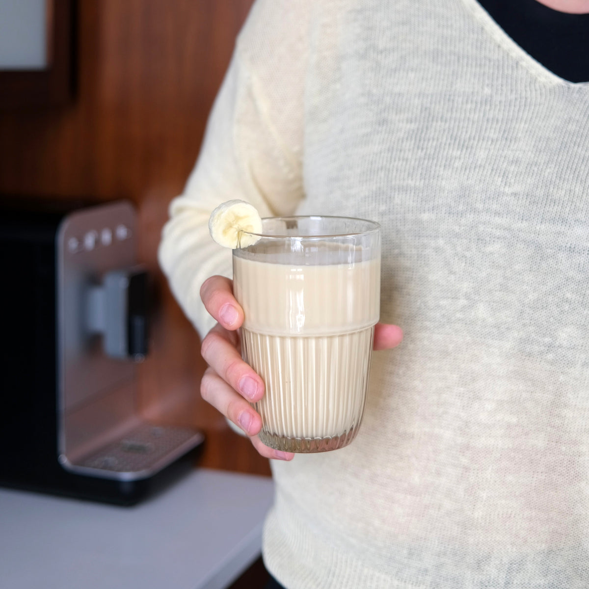 Person holding a glass of milkshake with an espresso machine in the background