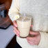 Person holding a glass of creamy beverage with a kitchen background