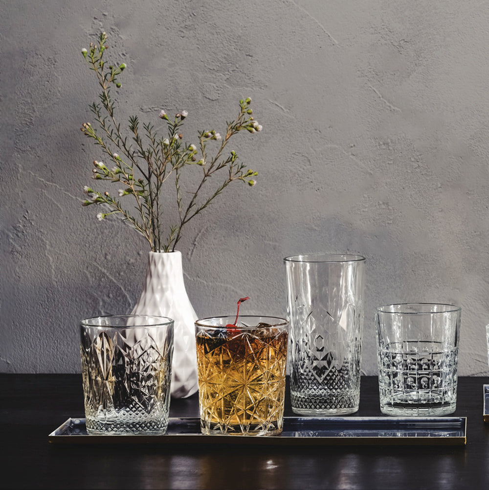 Assorted Bartender collection glasses on a table with a white vase with white flowers in the background