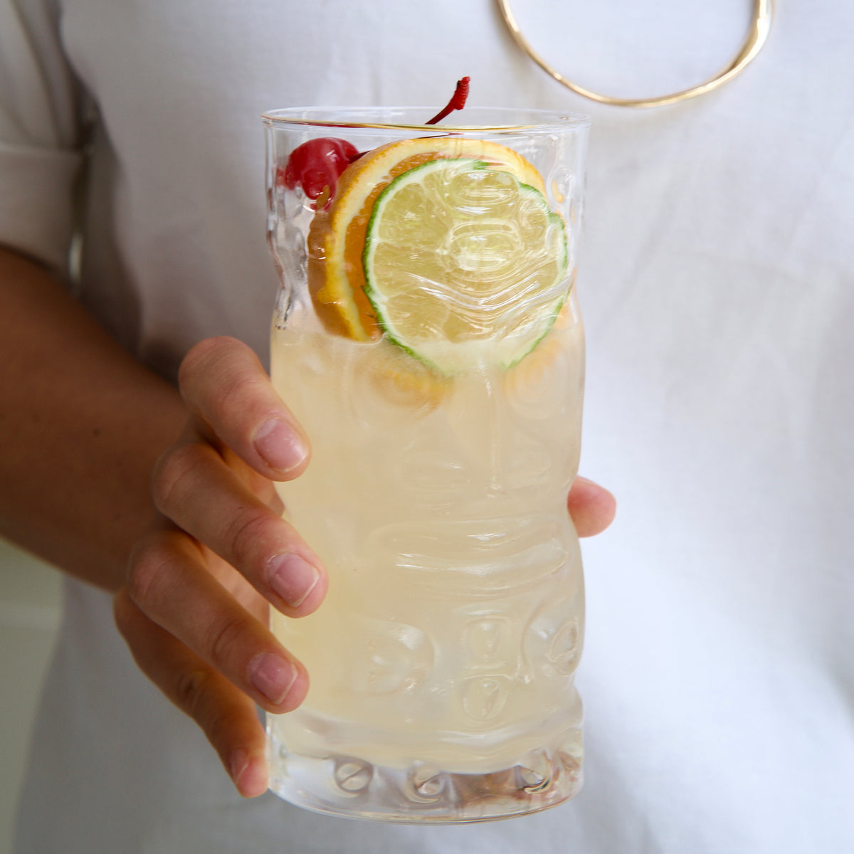 Hand holding a Bartender Tiki glass with Tiki cocktail with orange and lime slices on a white background