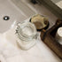 Glass jar with a metal clasp on a bathroom counter next to a soap dish with a bar of soap.