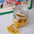 Glass jar with penne pasta on a white surface with a colorful box in the background