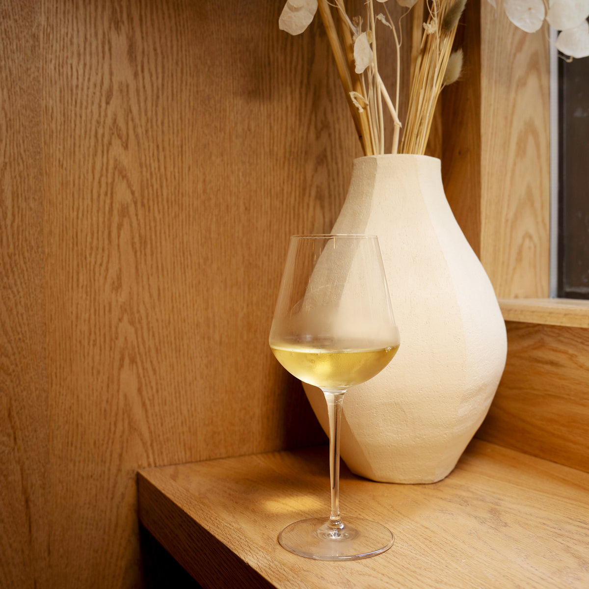 InAlto Uno Medium wine glass with white wine and a decorative vase on a wooden surface