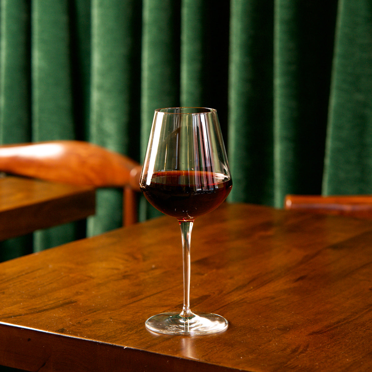 InAlto Uno Medium wine glass with red wine on a wooden table against a green curtain background